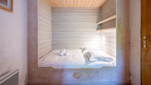 Uma cama de solteiro com roupa de cama branca e toalha, cabeceira de madeira e uma pequena prateleira acima da cama.