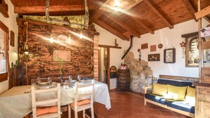 A rustic dining area with a wooden table set for four, a stone fireplace, and a wooden bench with cushions.