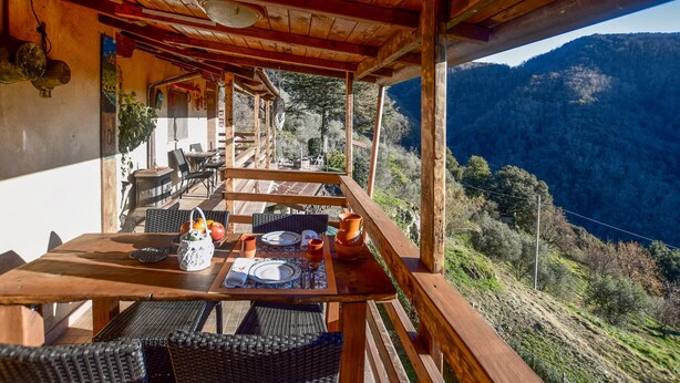 A wooden deck with a table set for dining, overlooking a mountainous landscape.