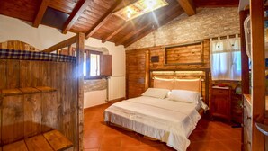 A rustic wooden bedroom with a large bed, a wooden bench, and a stone wall.