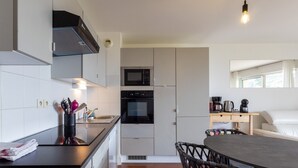 A compact kitchen with a microwave, oven, and sink, a dining area with a table and chairs, and a window with curtains.