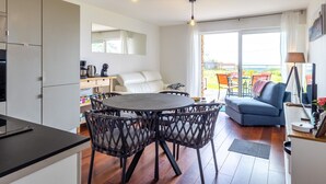 A modern kitchen with a dining area, a sofa, and a balcony with outdoor furniture.