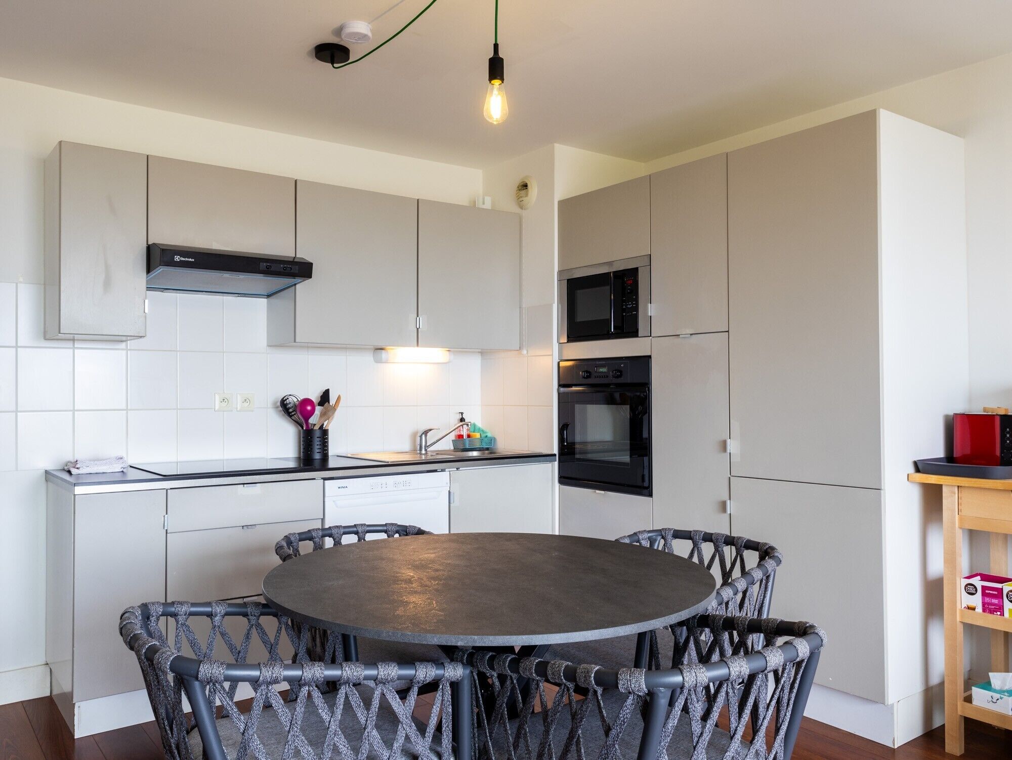 Una cocina moderna con una mesa redonda y sillas, electrodomésticos integrados y una lámpara colgante.