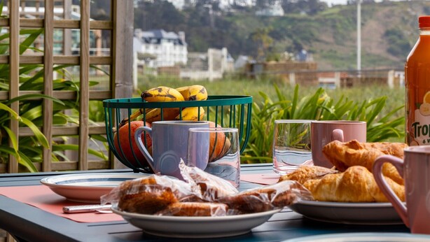 A breakfast table with a basket of bananas, a plate of pastries, and a bottle of orange juice.
