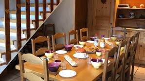 A dining area with a wooden table set for a meal, surrounded by chairs, and a wooden staircase with heart-shaped decorations.