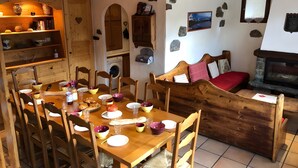 A cozy dining area with a wooden table set for a meal, a stone fireplace, and a stone wall with a framed picture.