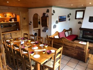 A cozy dining area with a wooden table set for a meal, a stone fireplace, and a stone wall with a framed picture.