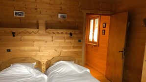 A wooden cabin room with two beds, a wooden door, and a small window.
