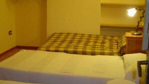 A room with two beds, a nightstand with a lamp, and a wall-mounted shelf.