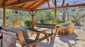 A covered outdoor seating area with wooden benches and a table, a rustic bar, and a view of a mountainous landscape. - Country House 'El Castellet De L'Ocaive' with Mountain View, Wi-Fi and Air Conditioning (Alicante)