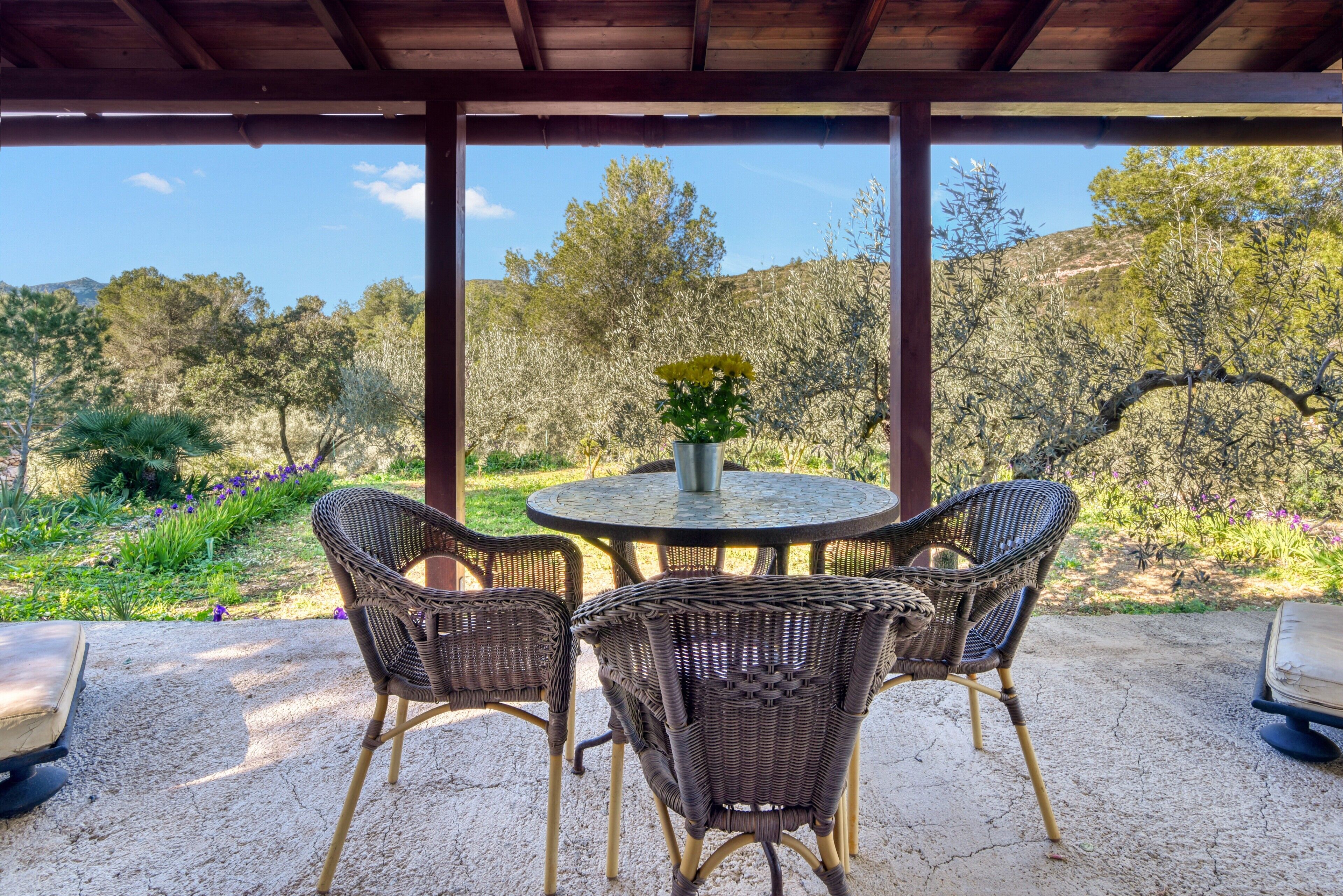 A covered patio with wicker chairs, a round table, and a vase of flowers.