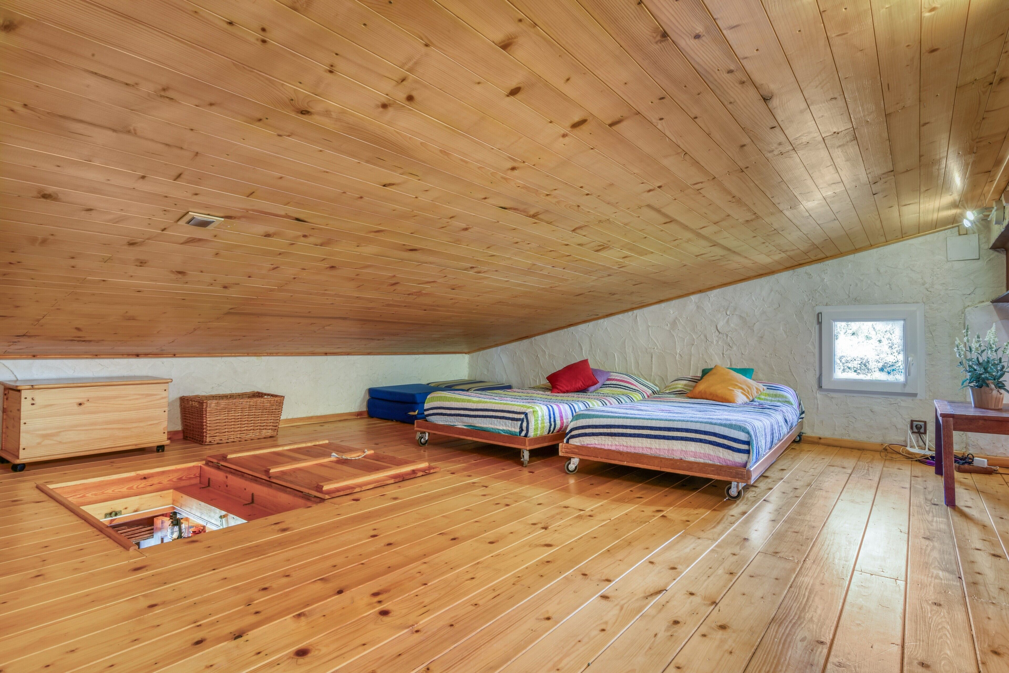 Dormitorio tipo loft con pisos de madera, dos camas, un aparador, una ventana y una mesita.