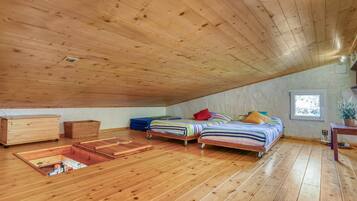 Dormitorio tipo loft con pisos de madera, dos camas, un aparador, una ventana y una mesita.