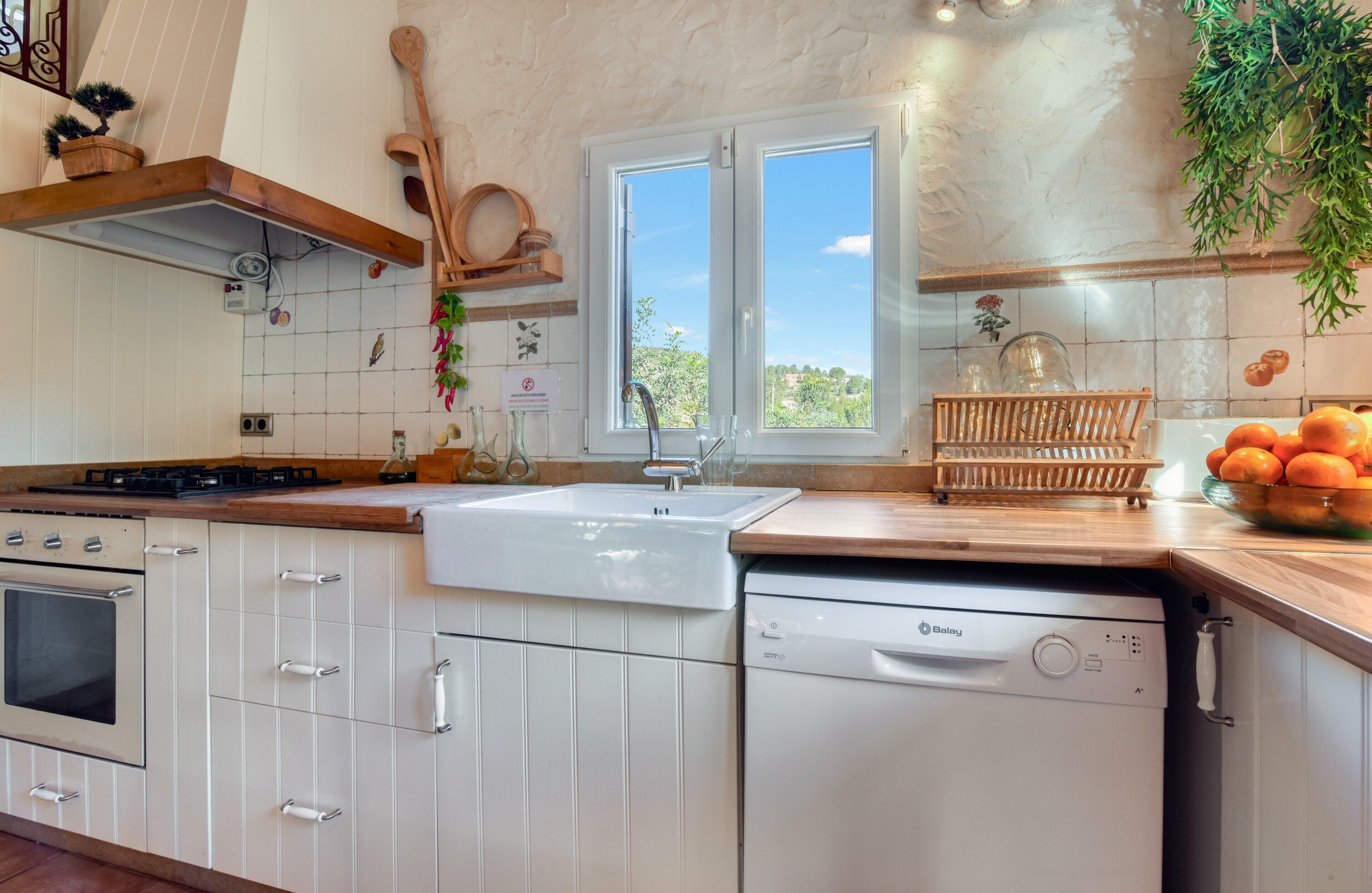 Una cocina con armarios blancos, lavavajillas, estufa y ventana con vistas.