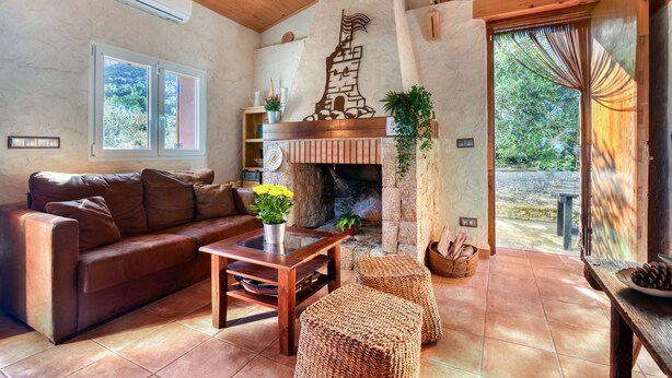 A cozy living room with a fireplace, a sofa, a coffee table, and wicker ottomans. - Country House 'El Castellet De L'Ocaive' with Mountain View, Wi-Fi and Air Conditioning (Alicante)