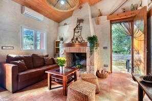 Una sala de estar acogedora con chimenea, un sofá, una mesita de centro y otomanas de mimbre.