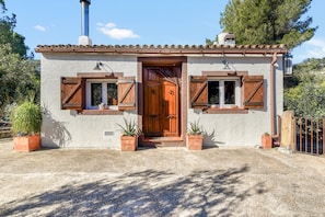 Un edificio rústico con tejado de tejas, puerta de madera y dos ventanas con contraventanas.
