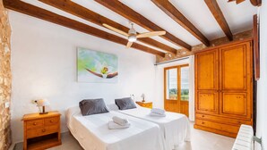 A bedroom with two beds, wooden ceiling beams, a painting, and a large wooden wardrobe. - Villa 'Pascual Gran' with Mountain View, Private Pool and Wi-Fi (Manacor)