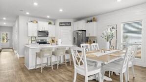 Une cuisine moderne avec des meubles blancs, un îlot central et un coin repas comprenant des chaises blanches et une table en bois.
