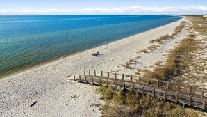 Une plage avec une promenade en bois qui mène à l’eau, un ciel dégagé et une mer calme.