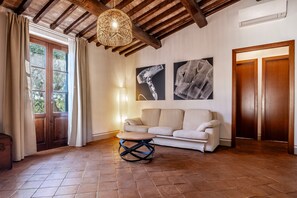 A room with a wooden ceiling, a round table, a sofa, and two framed artworks on the wall. - Apartment 'Leccino' with Shared Pool, Wi-Fi and Air Conditioning (Capalbio)