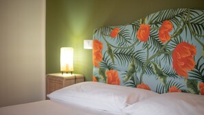 Ein Bett mit weißer Bettwäsche, ein Kopfstück mit Blumenmuster, ein Nachttisch mit Lampe und eine grüne Wand.
