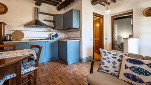 A kitchen with blue cabinets, a wooden ceiling, and a dining table with chairs. - Apartment 'Pendolino' with Shared Pool, Wi-Fi and Air Conditioning (Capalbio)