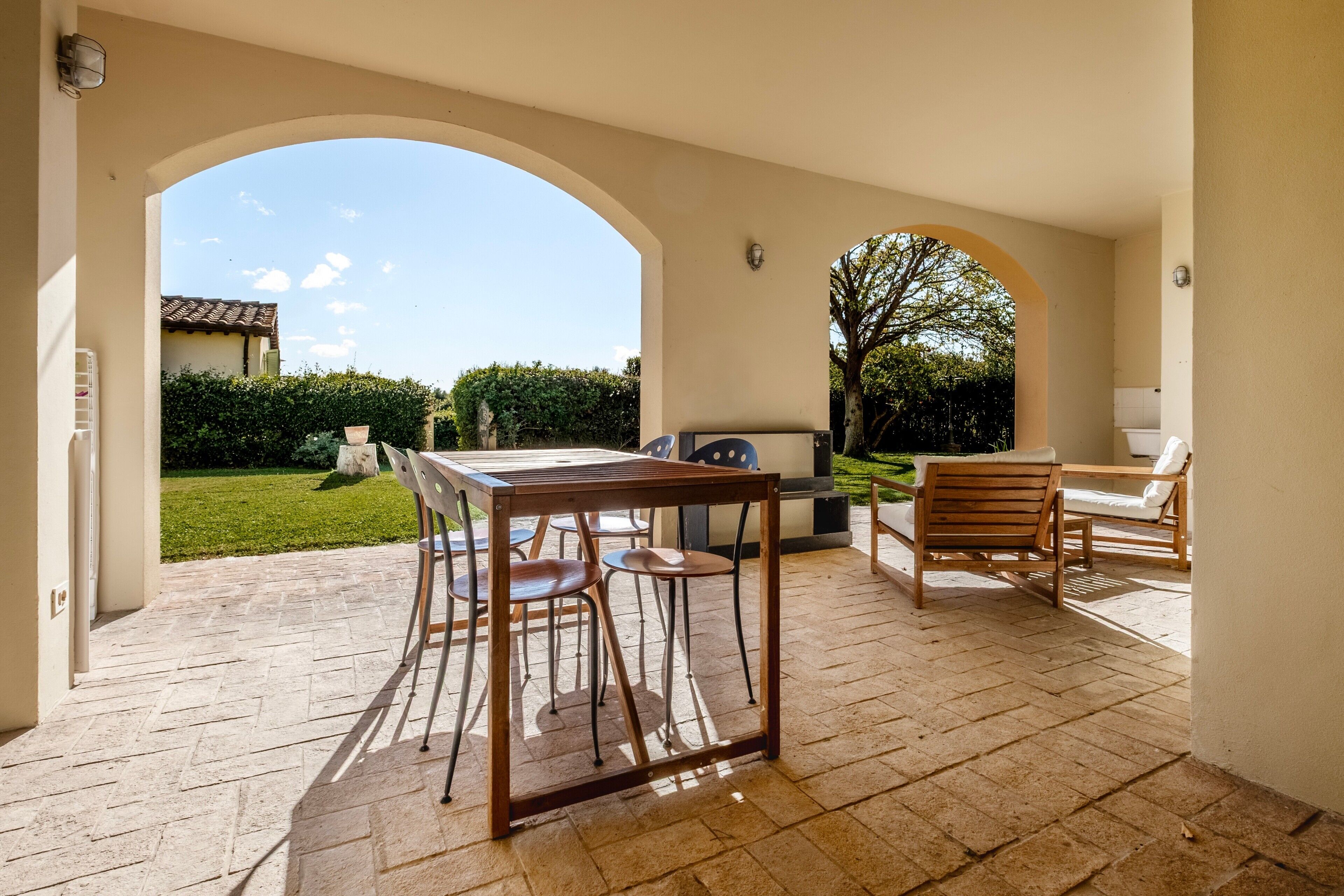 Une terrasse extérieure avec une table et des chaises, un barbecue et une vue sur une maison et un jardin.