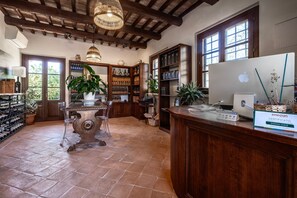 Ein geräumiges Zimmer mit Holzbalkendecke, einem großen Schreibtisch mit Computer, Regalen mit Flaschen und einem Weinkühlschrank.
