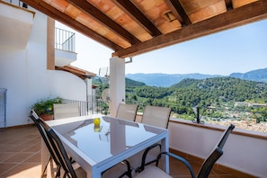 Een balkon met een tafel en stoelen, een potplant en uitzicht op een bergachtig landschap.