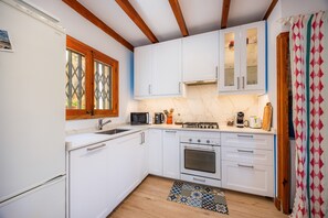 Een kleine keuken met witte kastjes, een magnetron, een fornuis en een spoelbak.