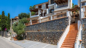 A multi-story building with a stone retaining wall, a staircase, and a balcony with outdoor furniture. - Apartment 'Sa Torreta Luxury Views' with Sea View, Private Terrace and Wi-Fi (Sóller)