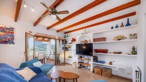 A modern living room with a sofa set, wooden beams, a ceiling fan, a TV, and shelves with various items. - Apartment 'Sa Torreta Luxury Views' with Sea View, Private Terrace and Wi-Fi (Sóller)