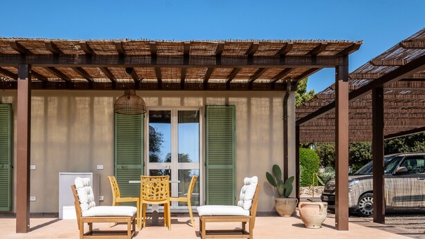 A covered patio with two wooden chairs and a table, a potted plant, and a car parked nearby. - Apartment '5' with Shared Pool, Wi-Fi and Air Conditioning (Capalbio)