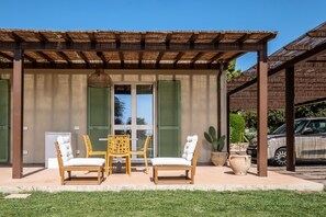 Une terrasse couverte avec deux chaises en bois et une table, une plante en pot et une voiture garée à proximité.