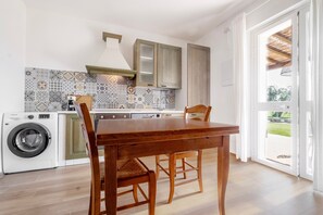 A kitchen with a wooden table, chairs, a washing machine, and patterned backsplash.