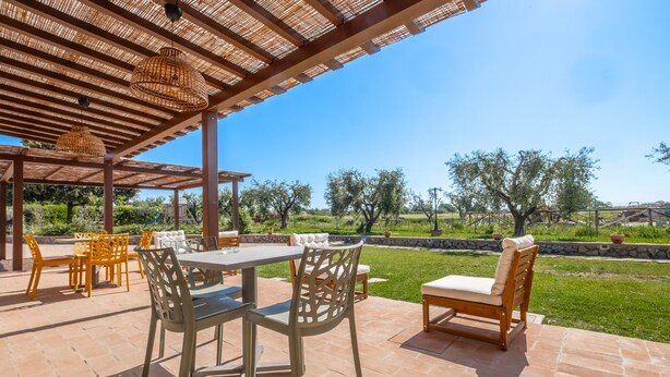En udendørs terrasse med borde og stole, en pergola og udsigt over landskabet.