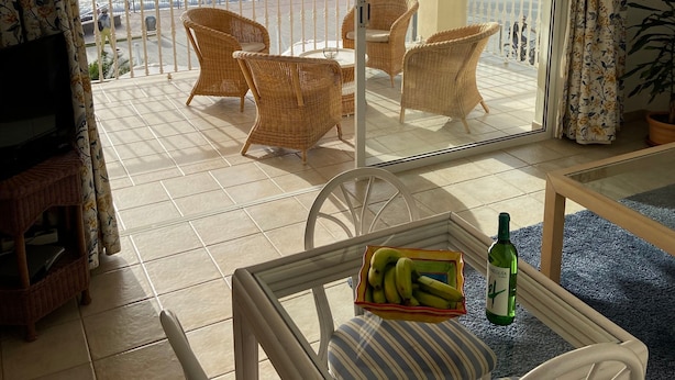 Un balcone con mobili in vimini, un tavolino in vetro con una bottiglia e delle banane, e vista sul mare.
