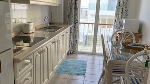 Cucina con mobili bianchi, un tostapane e un lavello. C'è un'area pranzo con tavolo e sedie, e vista all'esterno tramite una porta vetrata.