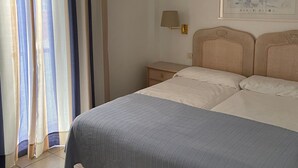 Una camera da letto con un letto, tende, un comodino, una lampada e un quadro appeso al muro.