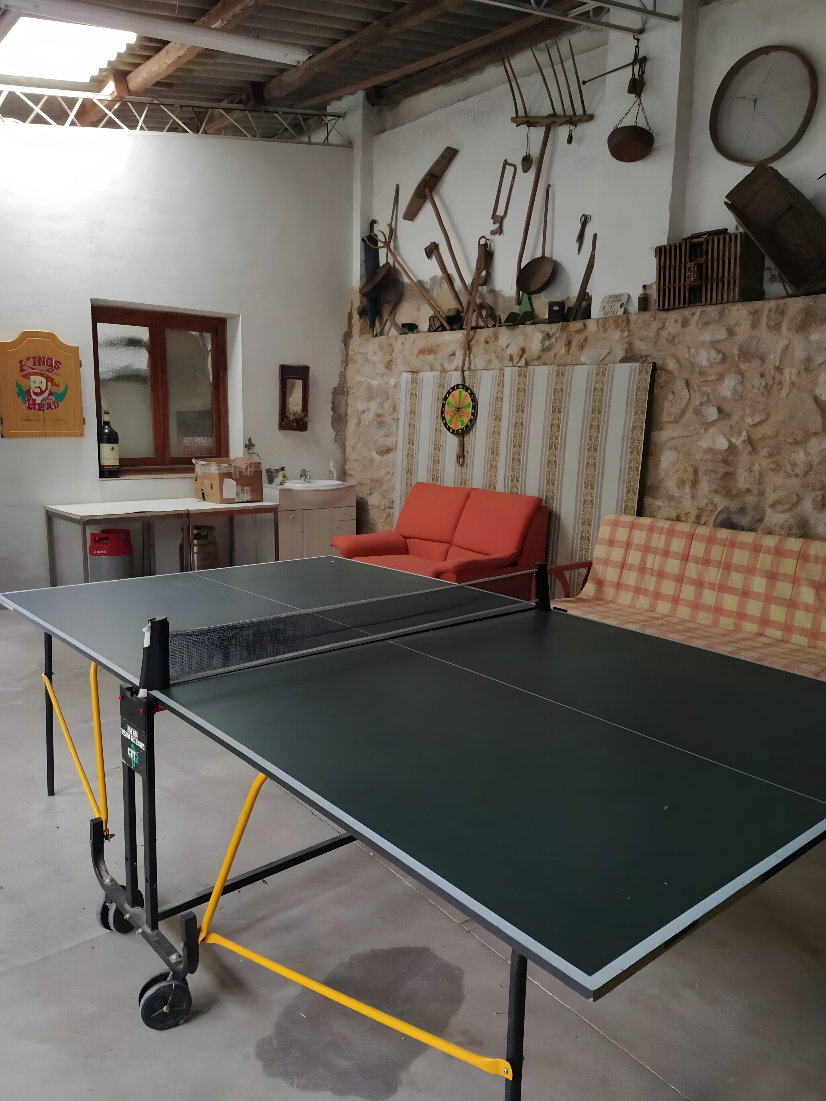 A ping pong table in a room with a stone wall, a window, and various tools hanging on the wall.