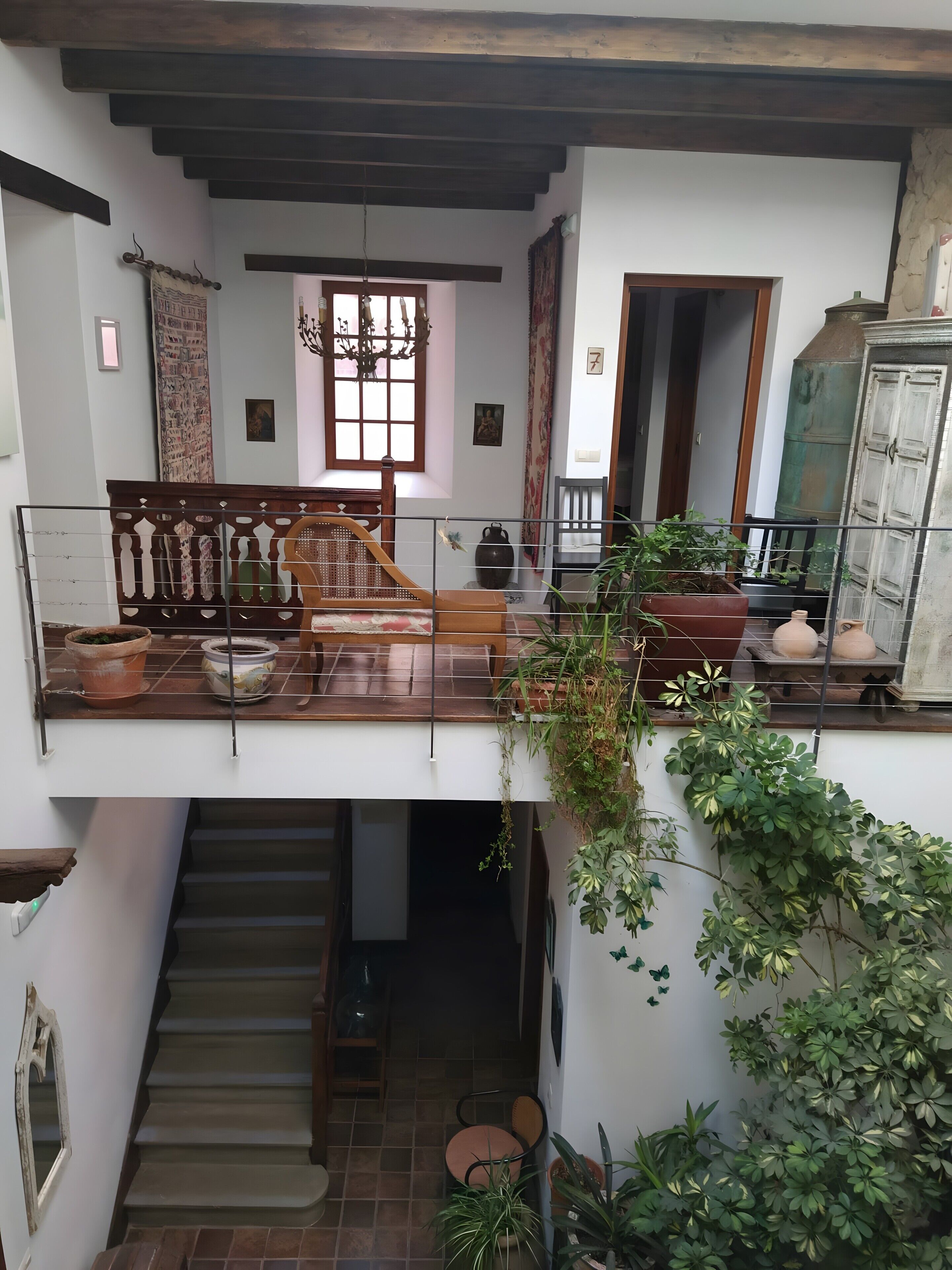 Un interior de varios niveles con escalera, muebles de madera y plantas en macetas.
