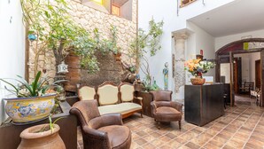 A cozy courtyard with a stone wall, a wooden bench, leather chairs, and potted plants.