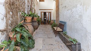 A narrow courtyard with potted plants, a wooden bench, and a door leading to an interior space.