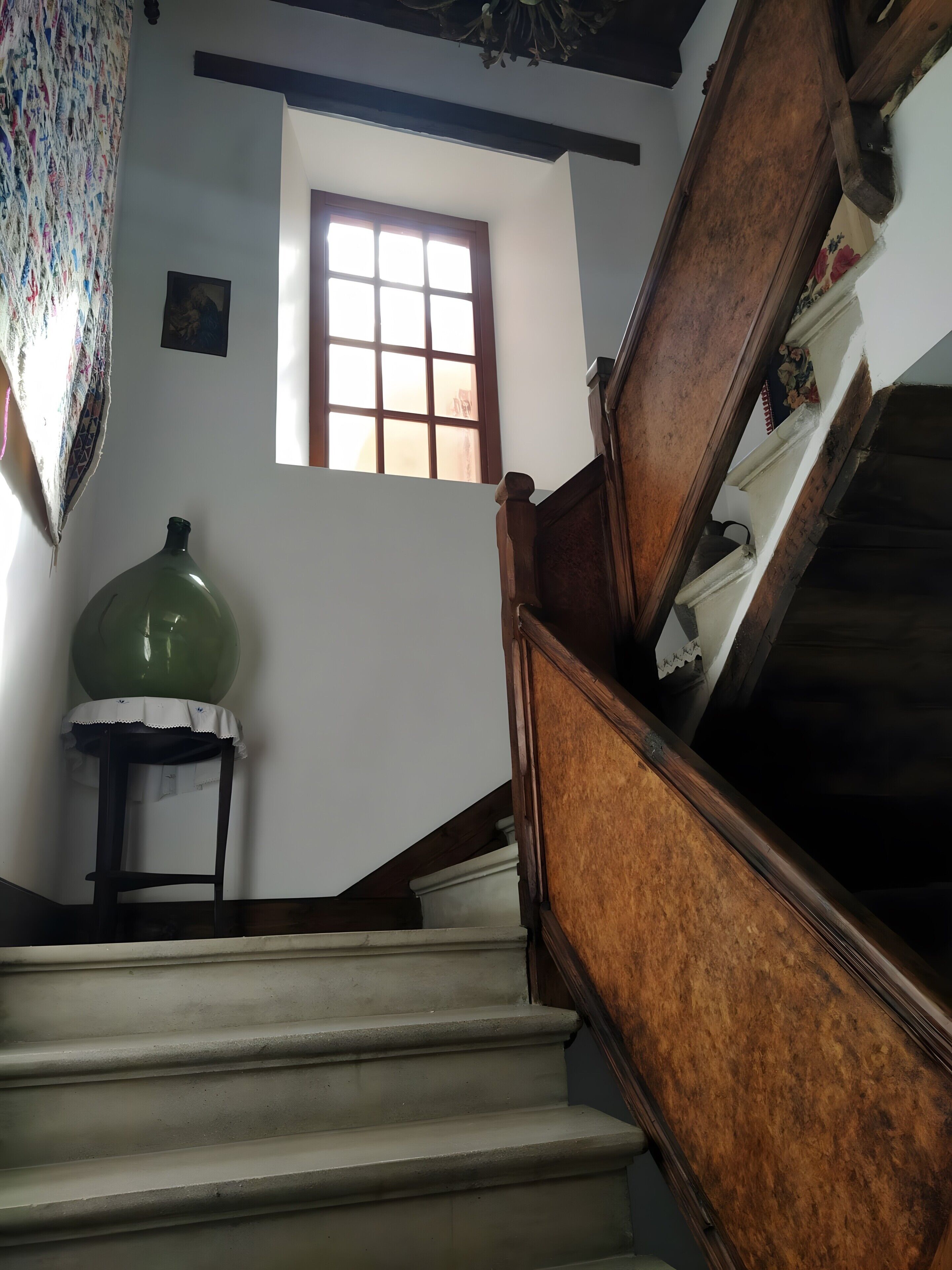 Eine Treppe mit hölzernen Geländern, ein grüner Blumentopf auf einem kleinen Tisch und ein Fenster mit Gitterverglasung.