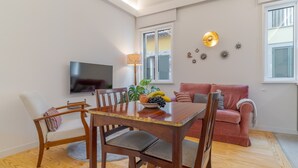 Una sala de estar moderna con una mesa de comedor, sillas, un sofá, un televisor y decoración mural.