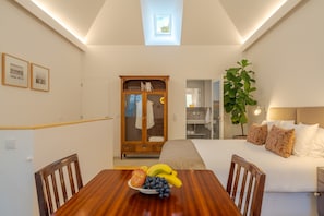 Quarto de hotel com mesa de jantar, cama, guarda-roupa e uma planta.
