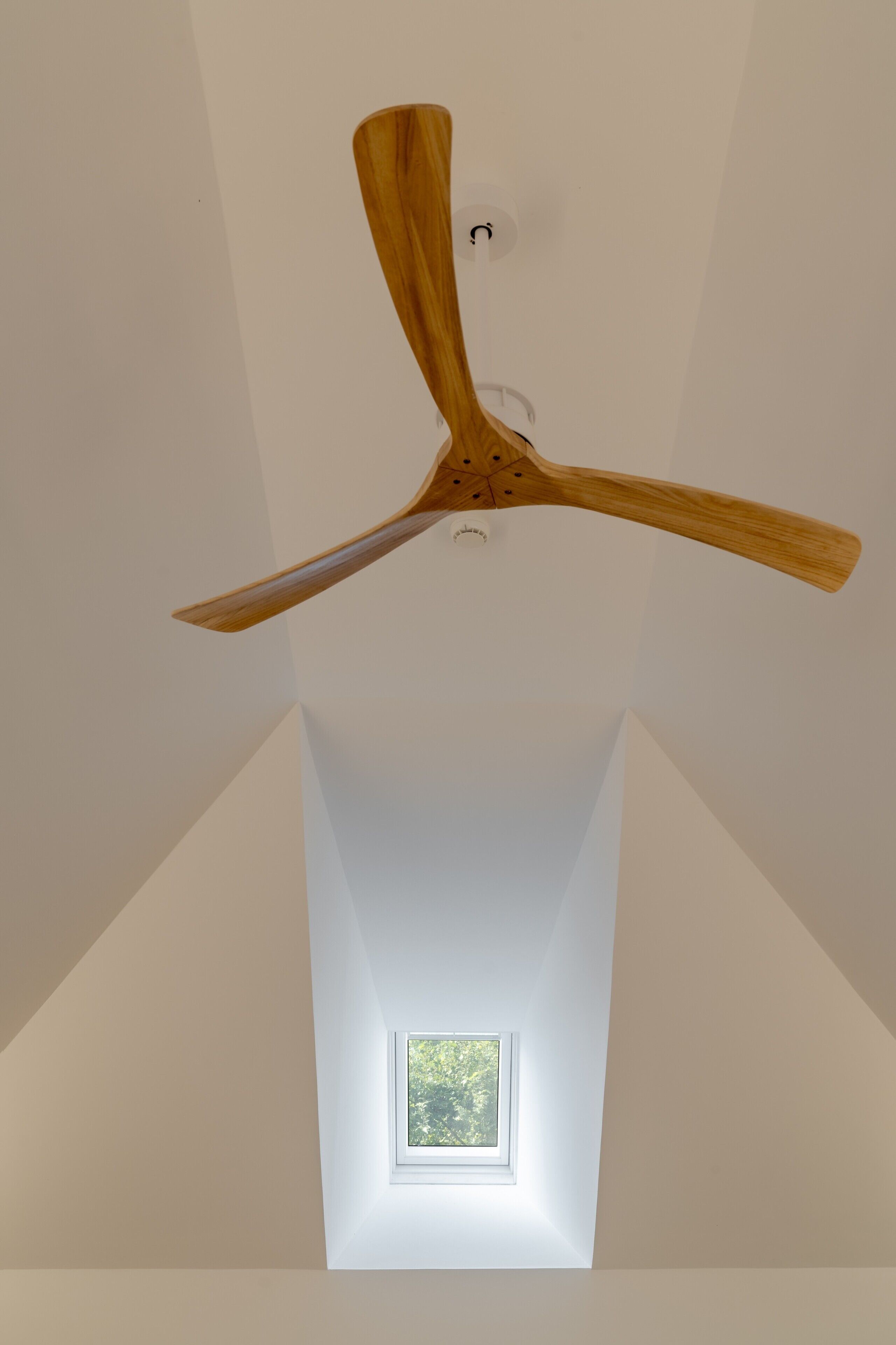 A ceiling fan with a wooden design in a room with a skylight and a small window.