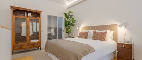 Un dormitorio con una cama grande, un armario de madera, una mesita de noche y una planta en maceta.