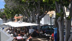 Un café al aire libre con mesas y sombrillas, rodeado de árboles y edificios.